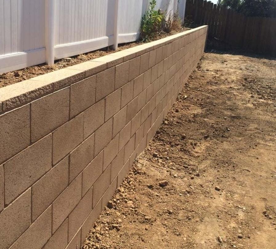 Straight retaining wall installation beside a fence